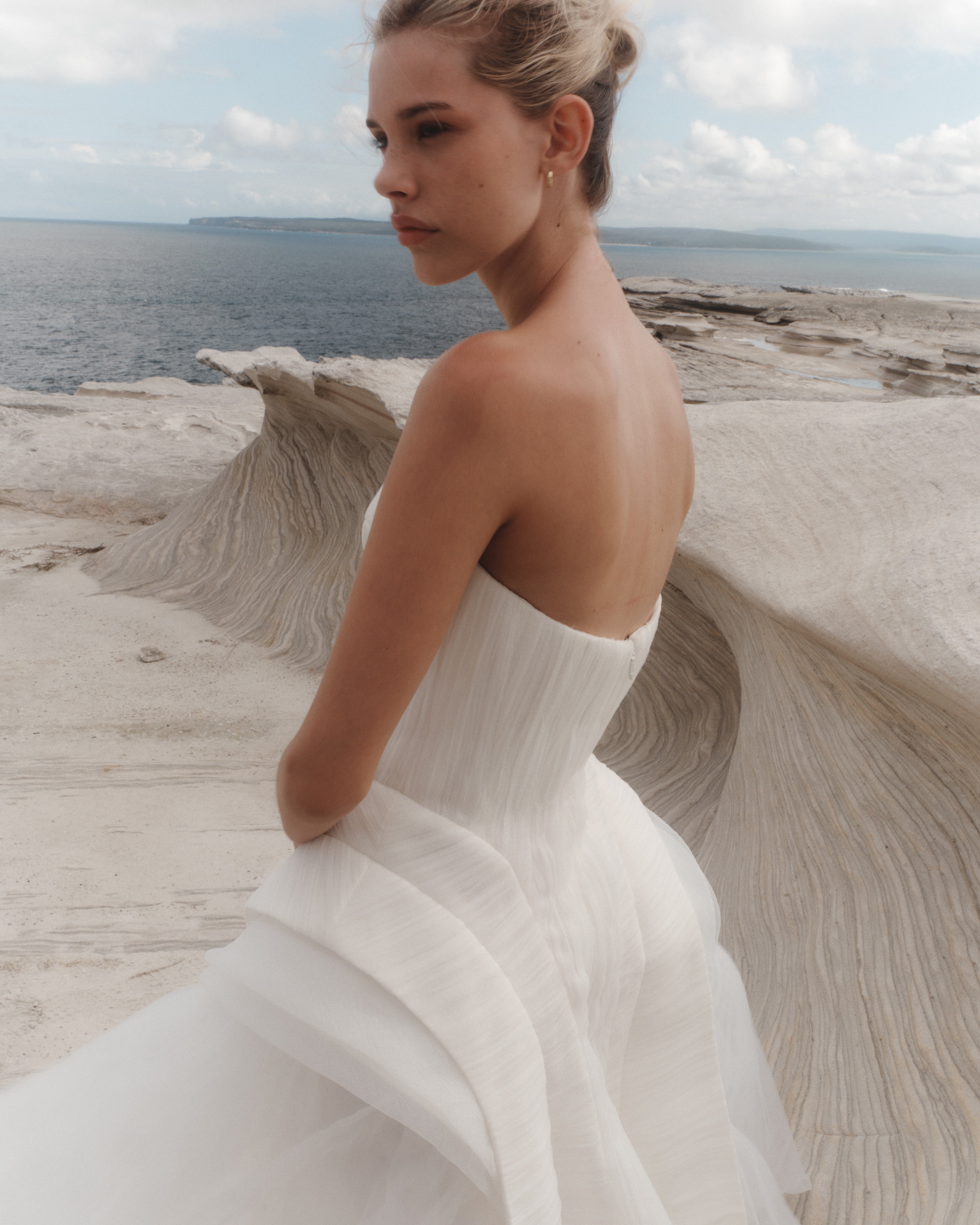 Woman in a white dress standing on a coastal landscape with ocean and sky in the background