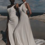 Two women in white dresses standing on a coastal cliff with ocean view.